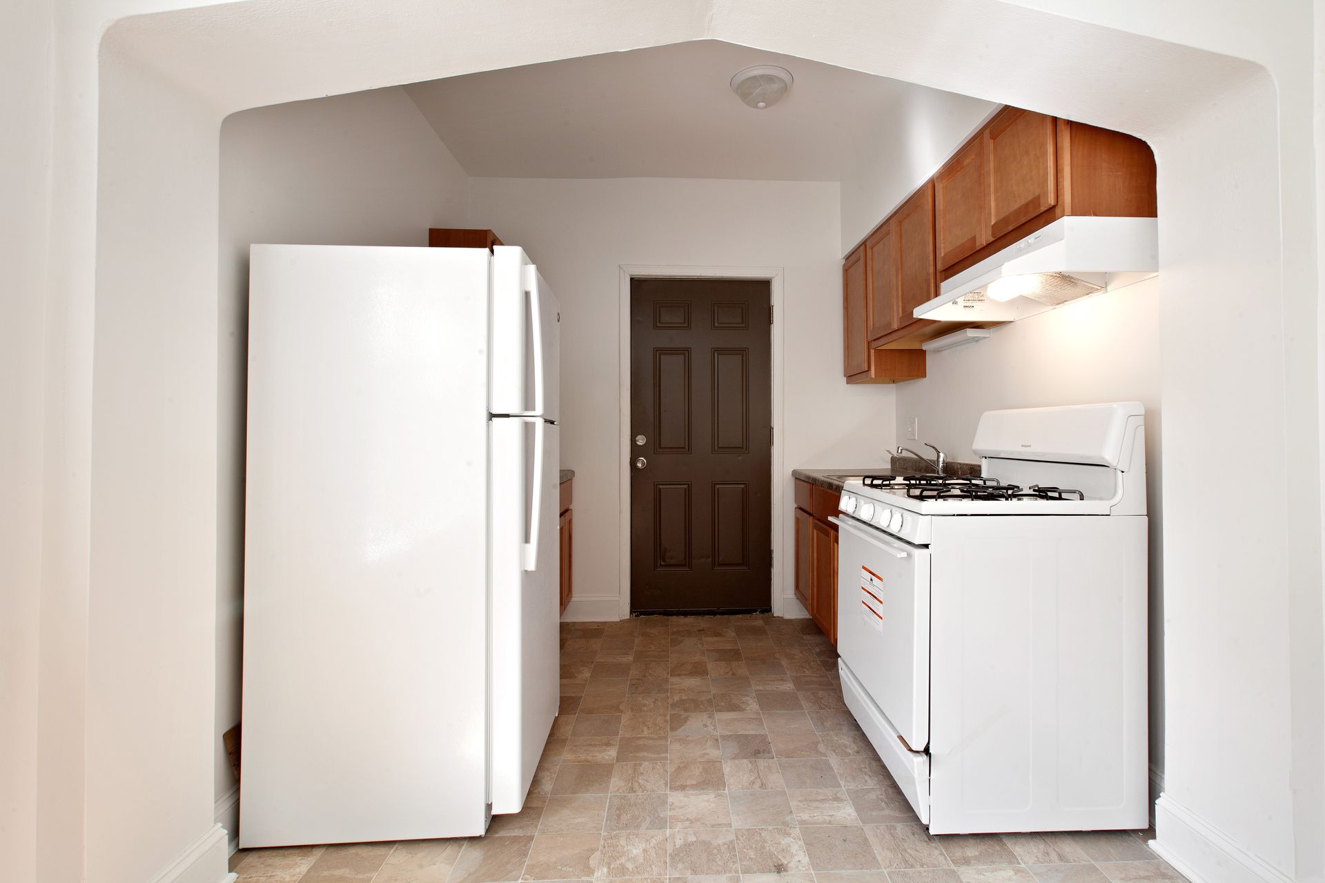 Kitchen with white appliances, brown cabinets, and a doorway.