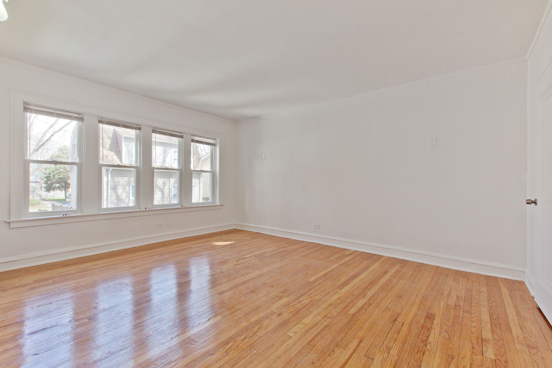 Empty room with hardwood floors, white walls, and a row of windows.