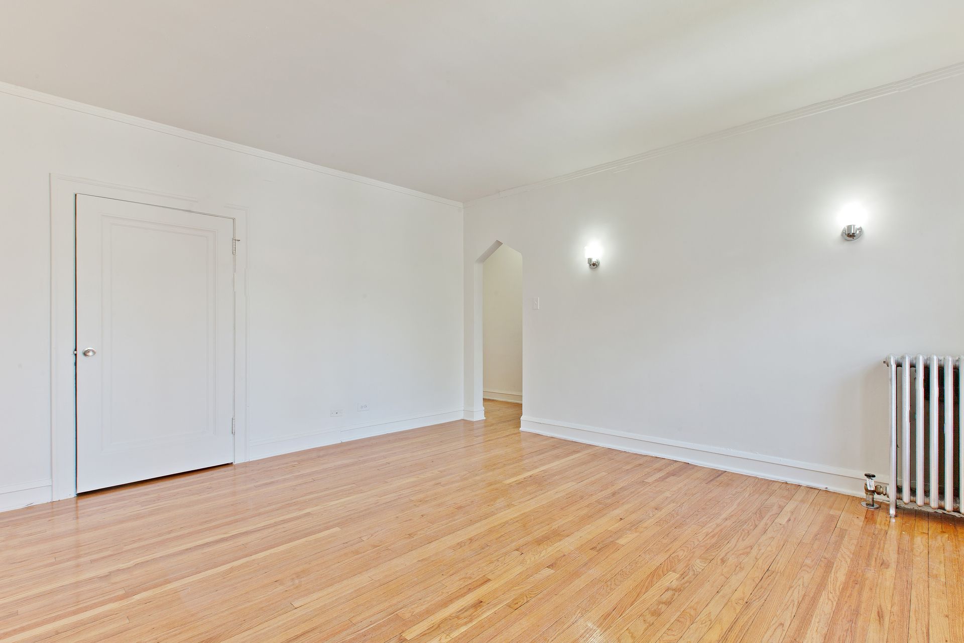 Empty room with light wood floors, white walls, and a radiator.