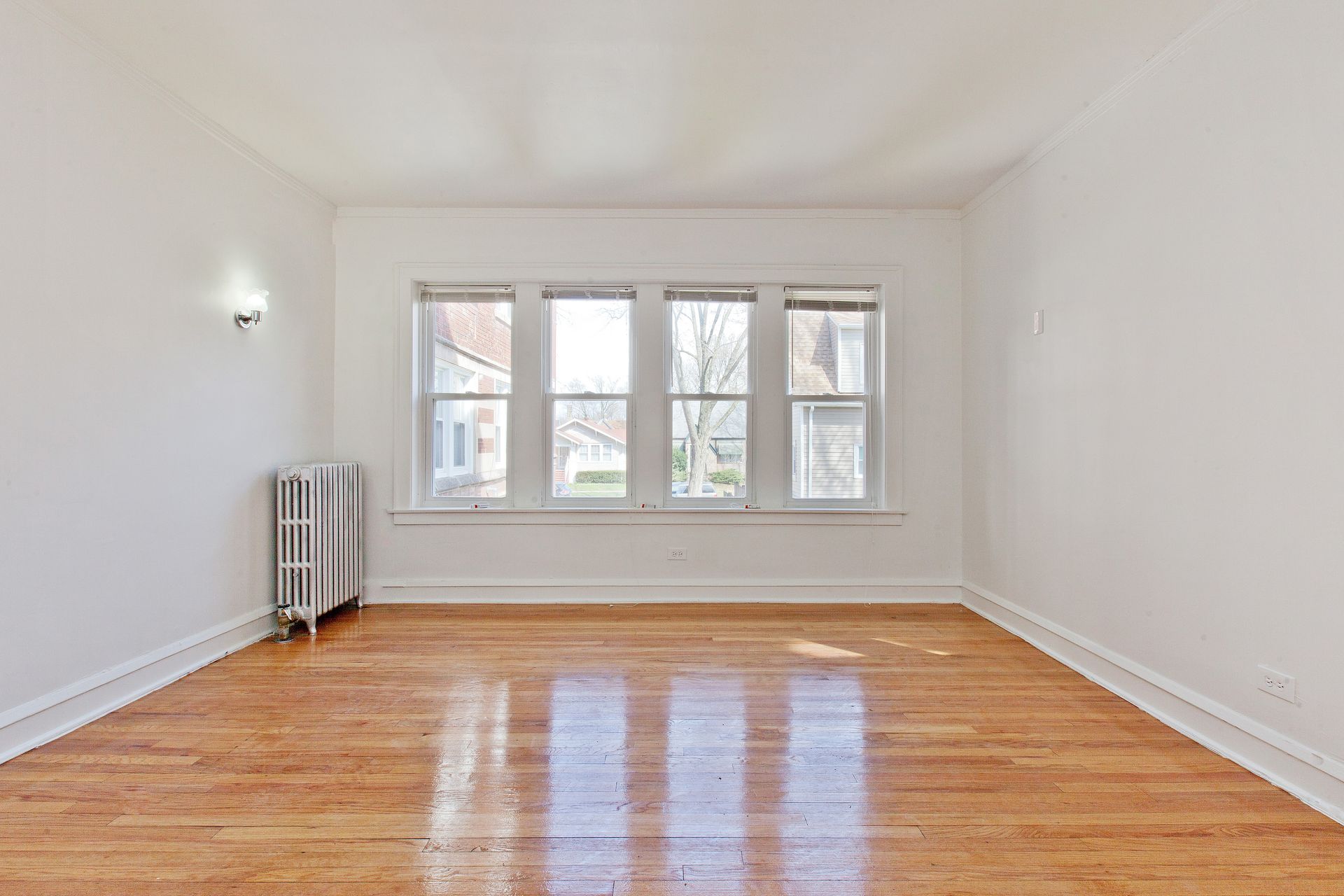Empty room with hardwood floors, a radiator, and large windows.