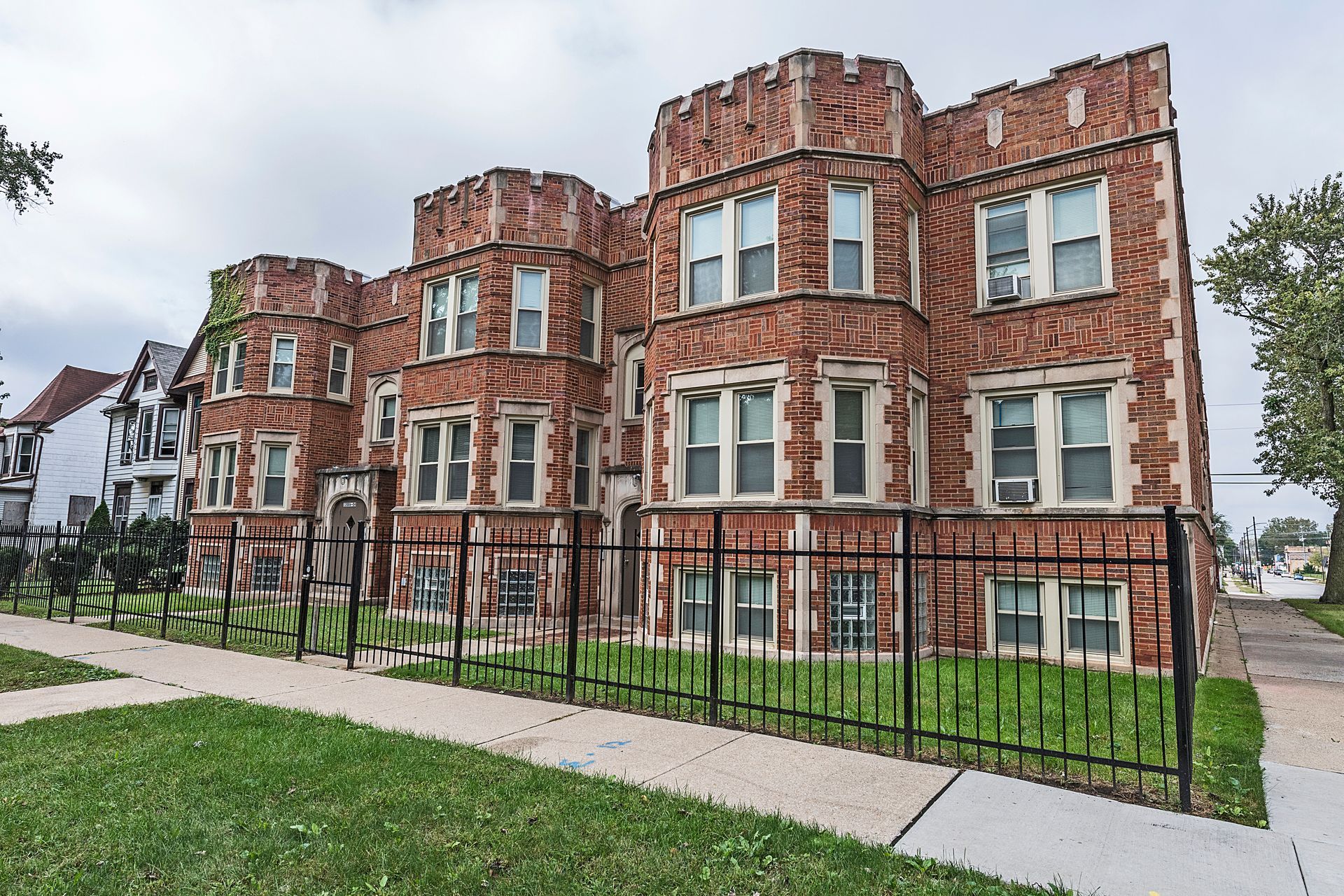 Red brick apartment building with decorative turrets and wrought iron fence.