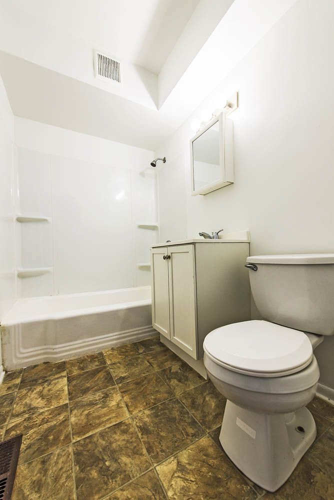 A small, white bathroom with a tub, toilet, vanity, and brown patterned flooring.