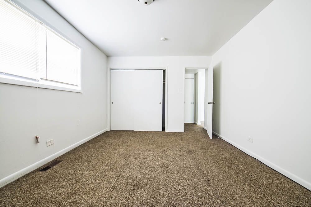 Empty bedroom with brown carpet, white walls, closet, and a window.