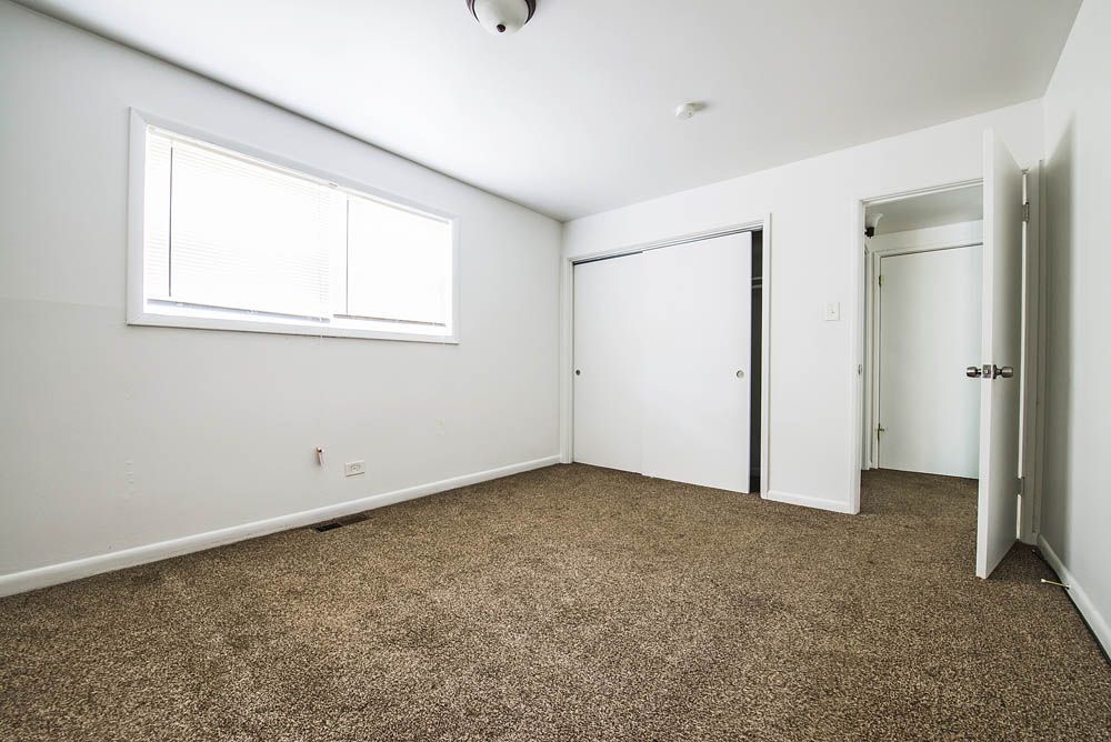 Empty room with white walls, window, closet, and open doorway, brown carpet.