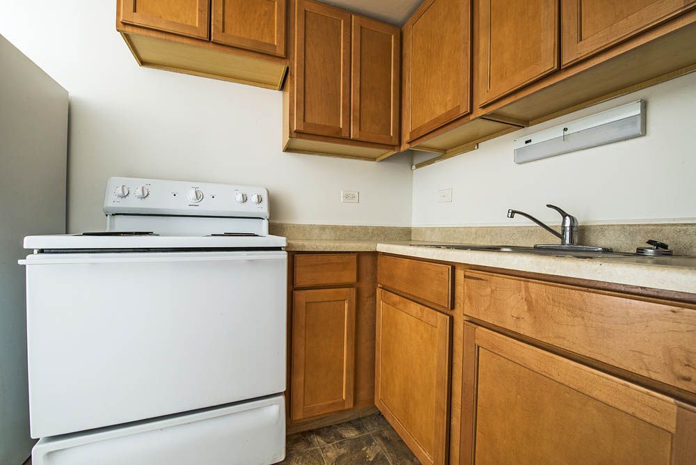 Small kitchen with wooden cabinets, white stove, and sink.