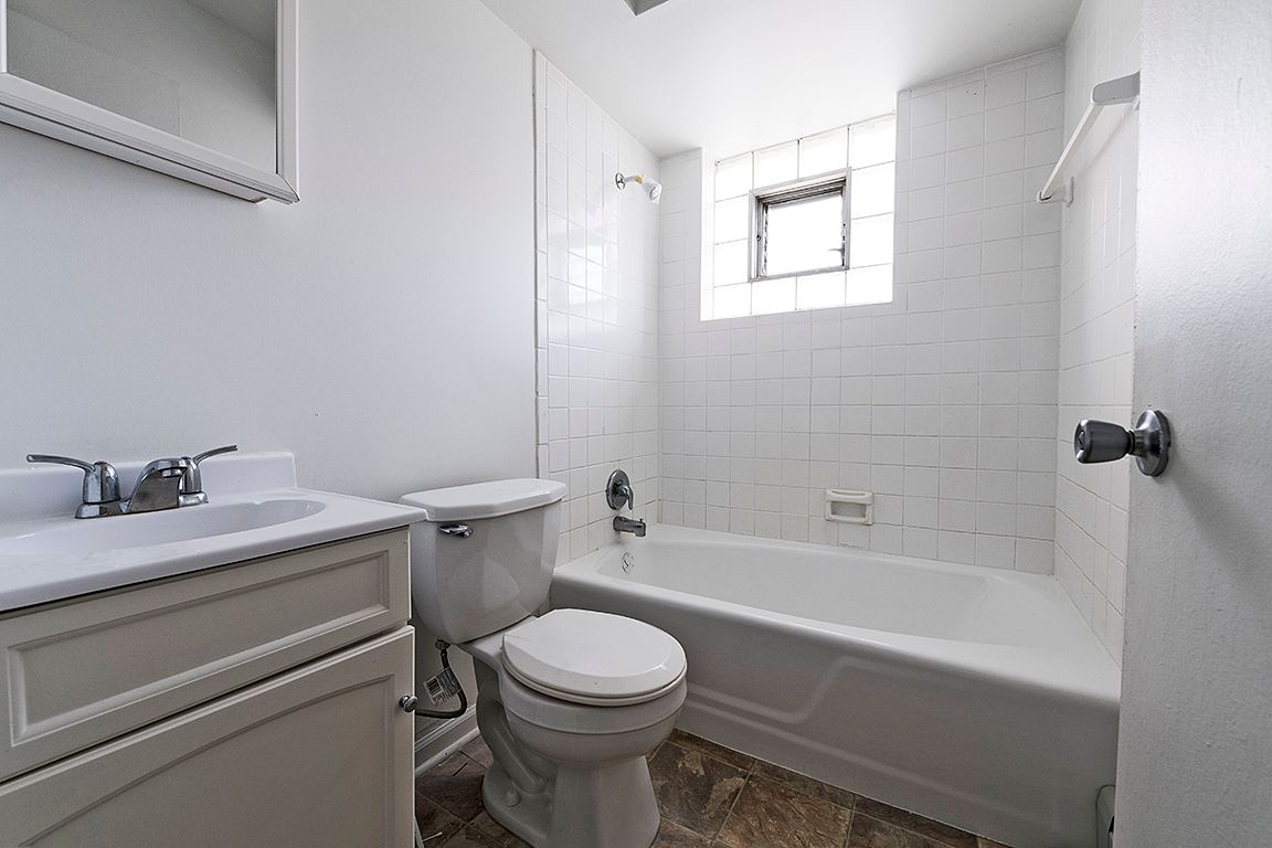 White bathroom with a sink, toilet, and bathtub. Small window above the tub.