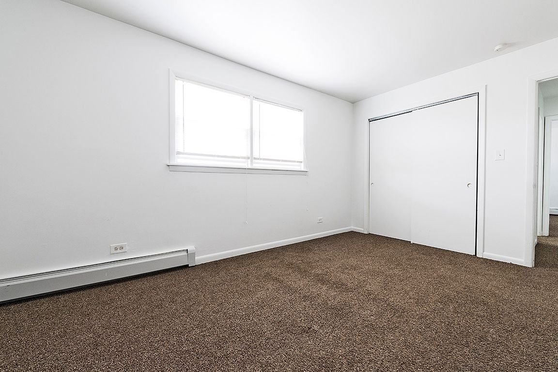 Empty room with white walls, brown carpet, window, and closet.