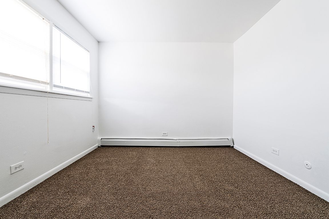 Empty room with brown carpet, white walls, and a window on the left.