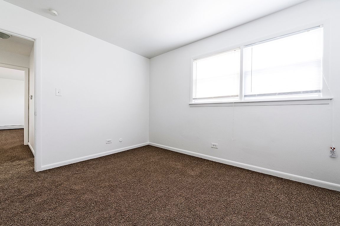 Empty room with brown carpet, white walls, and a window.