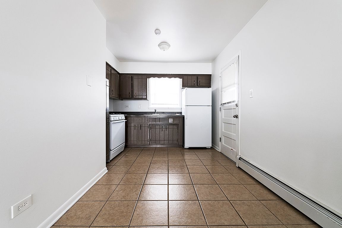 Empty kitchen with brown cabinets, white appliances, and tiled floor.