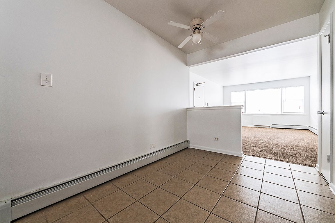 Empty room with tile floor, white walls, and a view into a carpeted room with a large window.