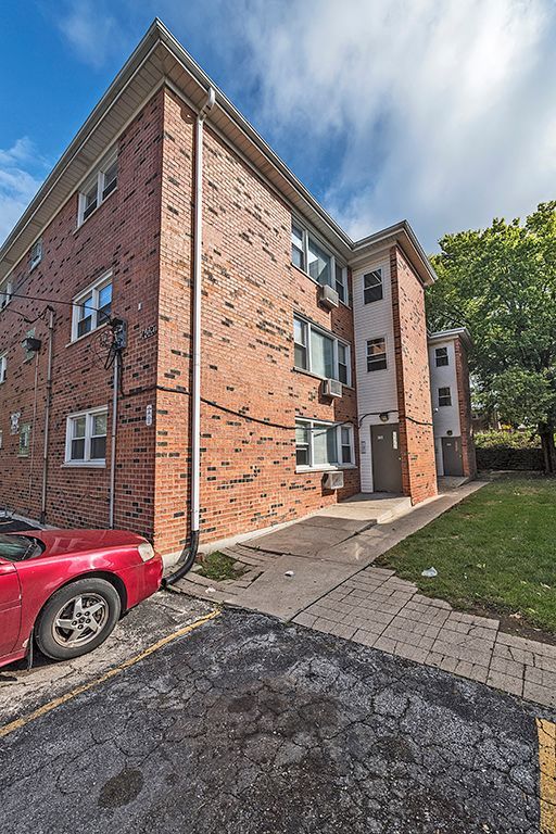 Red brick apartment building with white window frames and a red car parked nearby.
