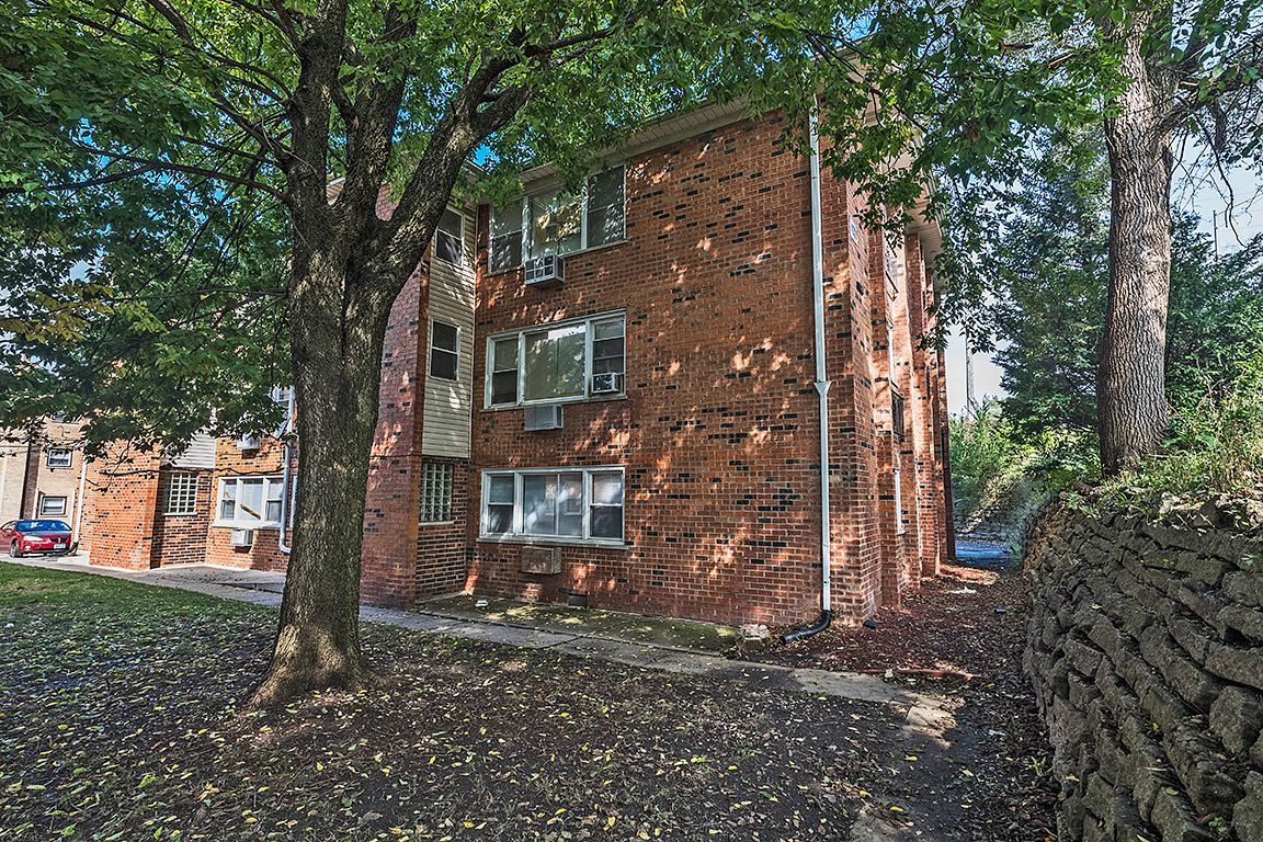 Brick apartment building partially obscured by trees.