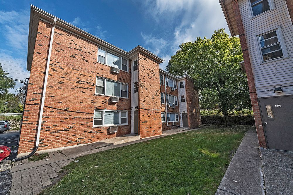 Red brick apartment building with white windows, green lawn, and blue sky.