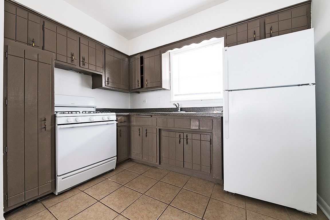 A small kitchen with brown cabinets, white appliances, and a window.
