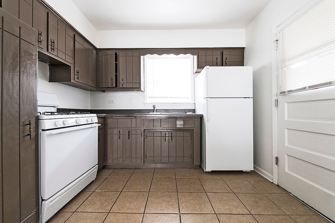 Brown cabinets, white appliances, and tiled floor in a kitchen with a window and a door.