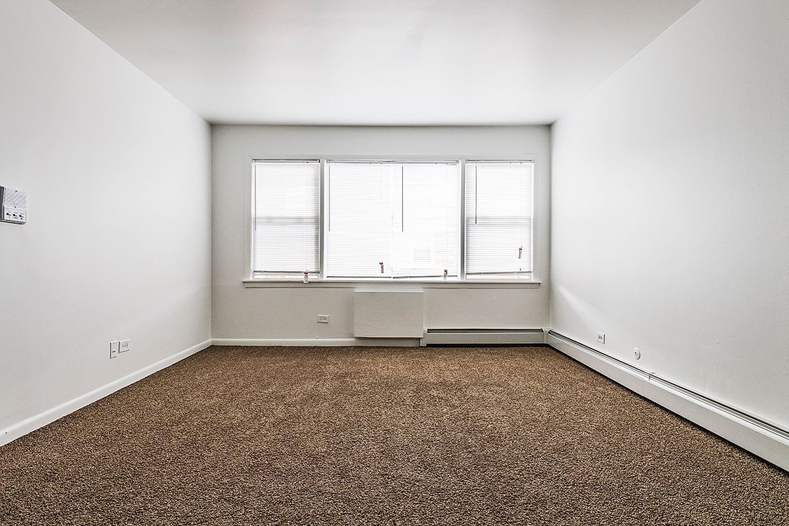 Empty room with brown carpet, white walls, and a window with blinds.