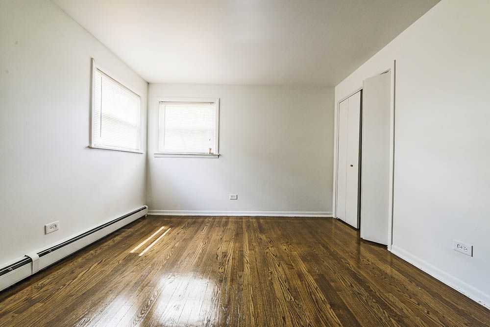 Empty room with hardwood floors, white walls, two windows, and closet doors.