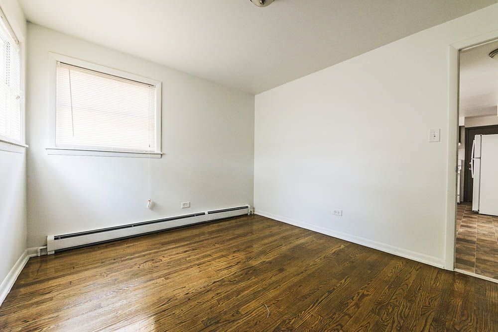 Empty room with hardwood floors, a window with blinds, and a doorway.