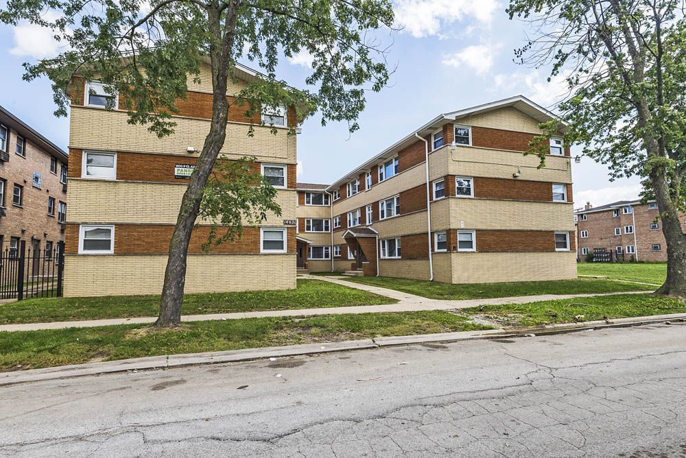 Multi-story brick apartment buildings with green lawns and trees.