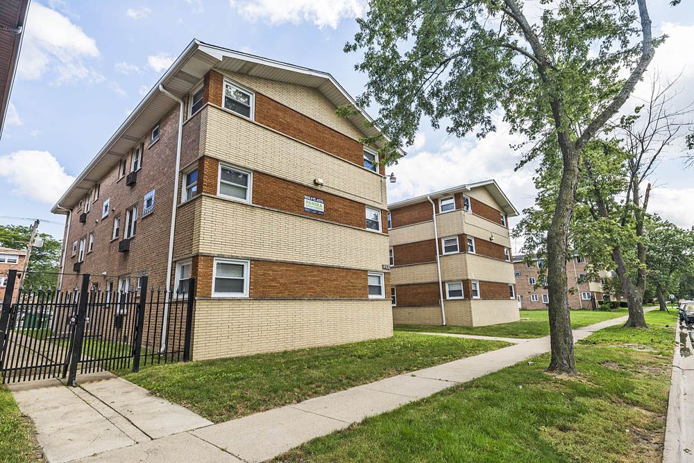 Two brick apartment buildings with light-colored siding, sidewalk, and green lawn.