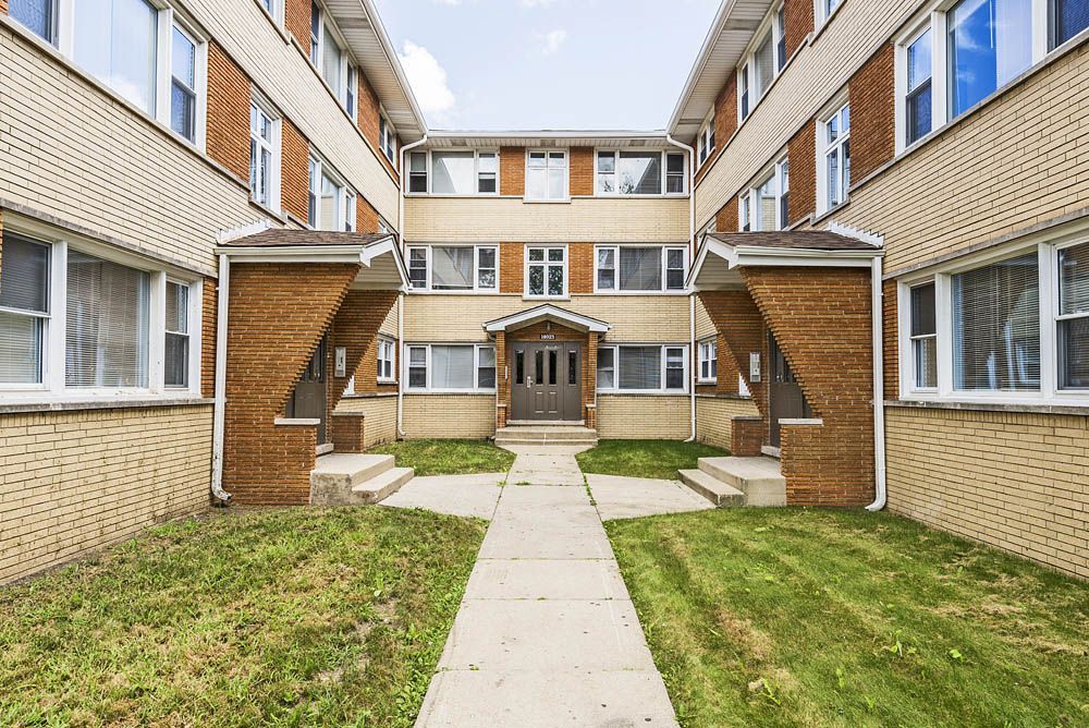 Apartment building exterior, red brick and beige walls, walkway leads to the entrance.
