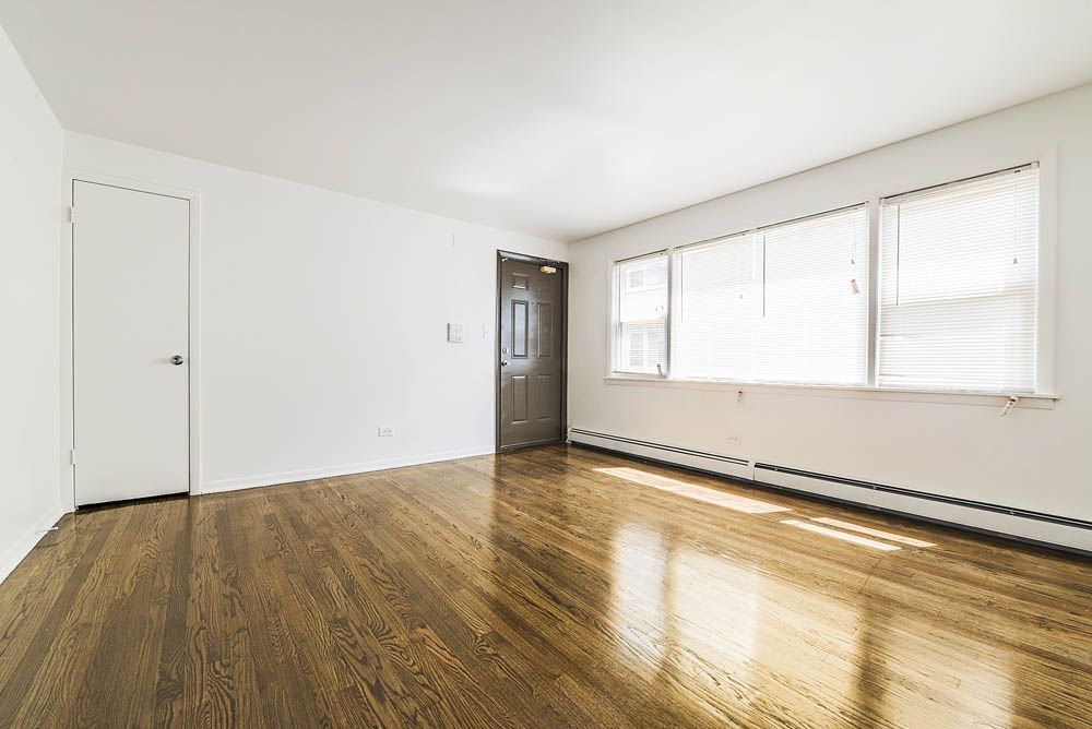 Empty room with hardwood floors, white walls, and a large window.