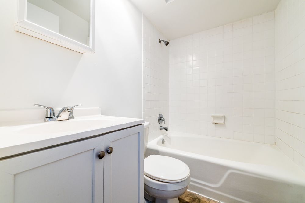 White bathroom with sink, toilet, bathtub, and mirror.