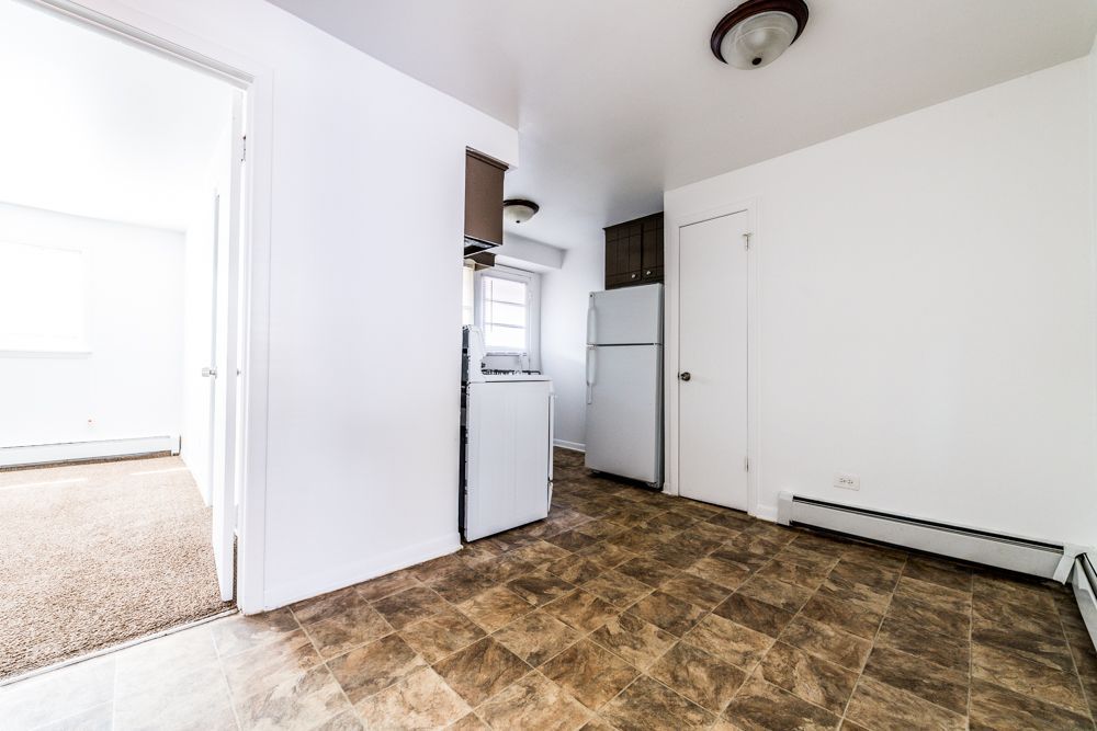 Empty kitchen with appliances. White walls, brown floor, open doorway to carpeted room.