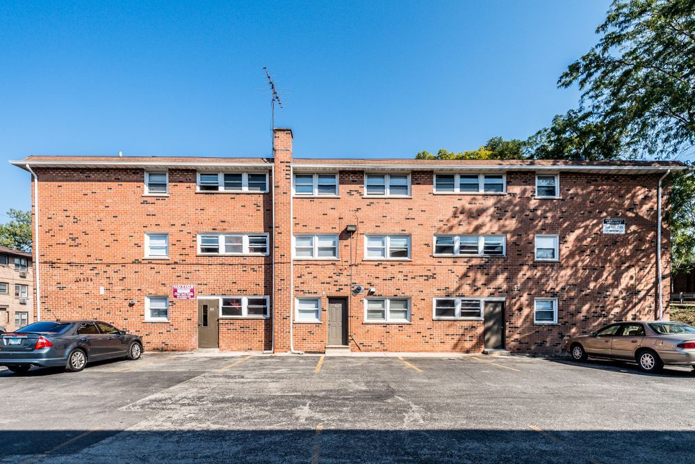 Brick apartment building with parking; two stories, brown car parked on the left, beige car parked on the right.