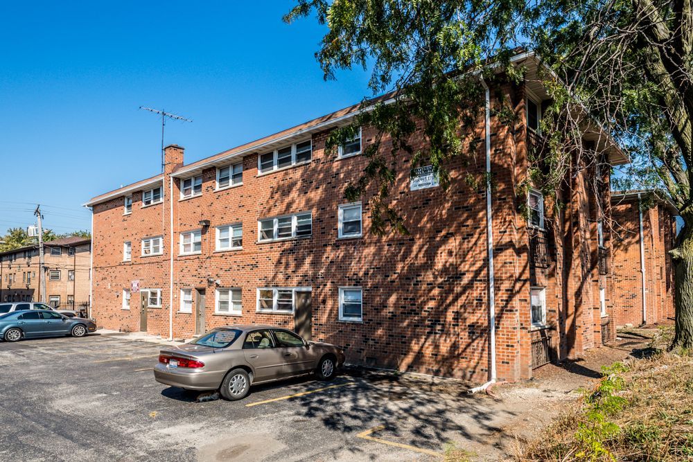 Brick apartment building with parked cars on a sunny day.