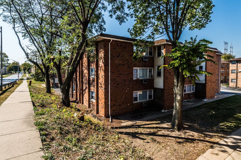 Brick apartment building with trees, sidewalk, and road.