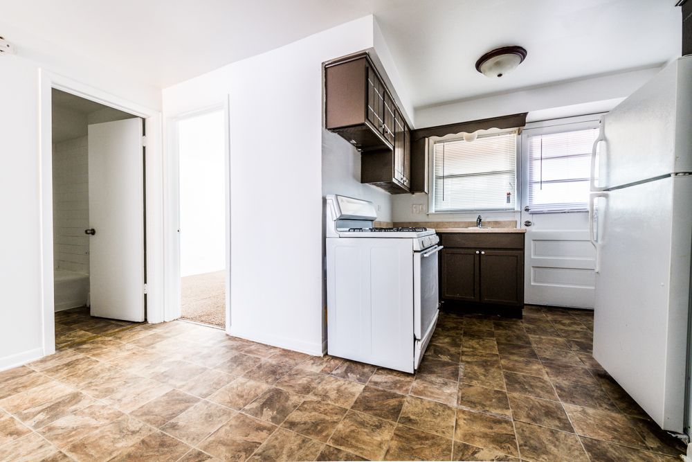 Kitchen with white appliances, brown cabinets and flooring, and a doorway.