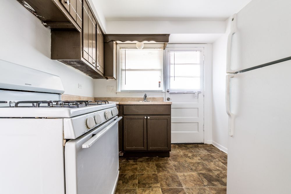 Kitchen with white appliances, brown cabinets and floor, and a door to the outside.