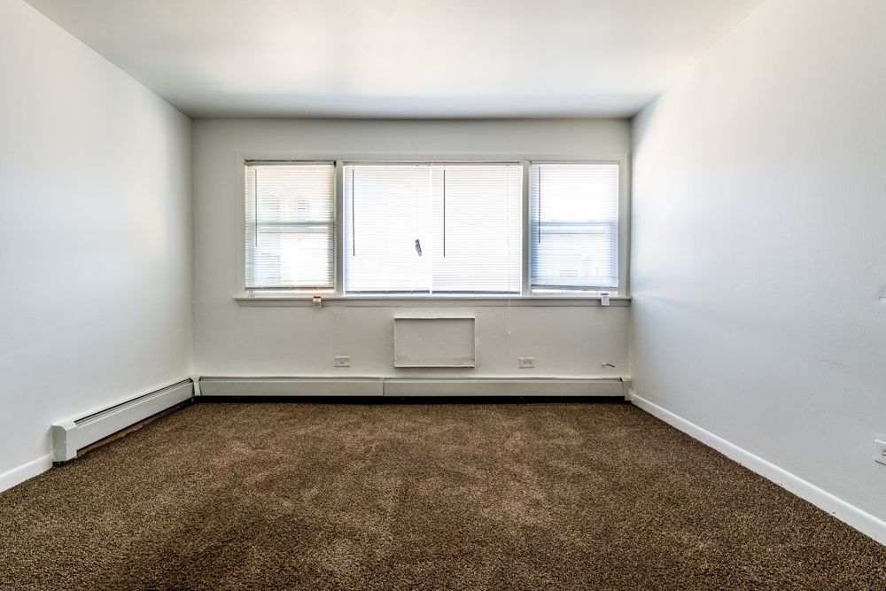 Empty room with brown carpet, white walls, and a window with blinds.