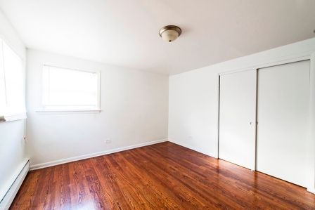 Empty room with hardwood floors, white walls, closet, and a window.