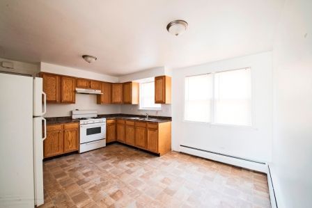 Empty kitchen with light brown cabinets, white appliances, and linoleum floor.