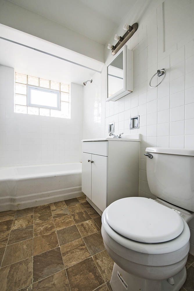 Small, white bathroom with tub, toilet, vanity, and brown tile floor.