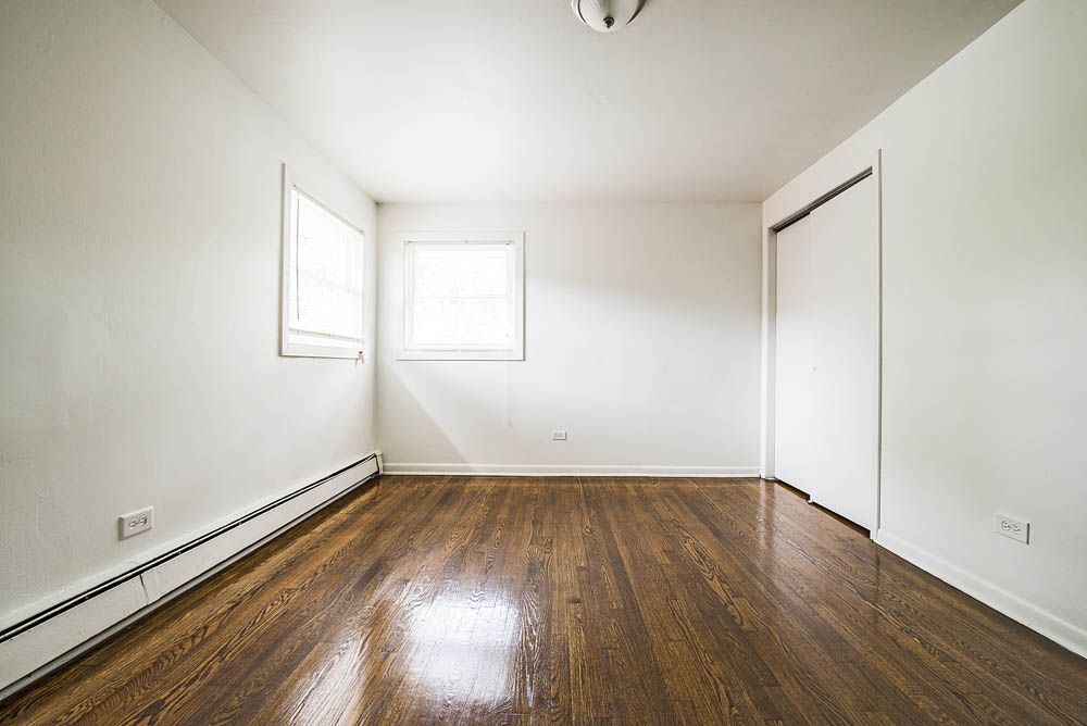 Empty room with hardwood floors, white walls, two windows, and closet.