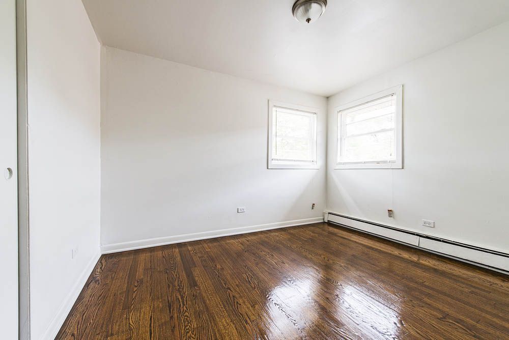 Empty room with hardwood floors, white walls, two windows, and a closet door.