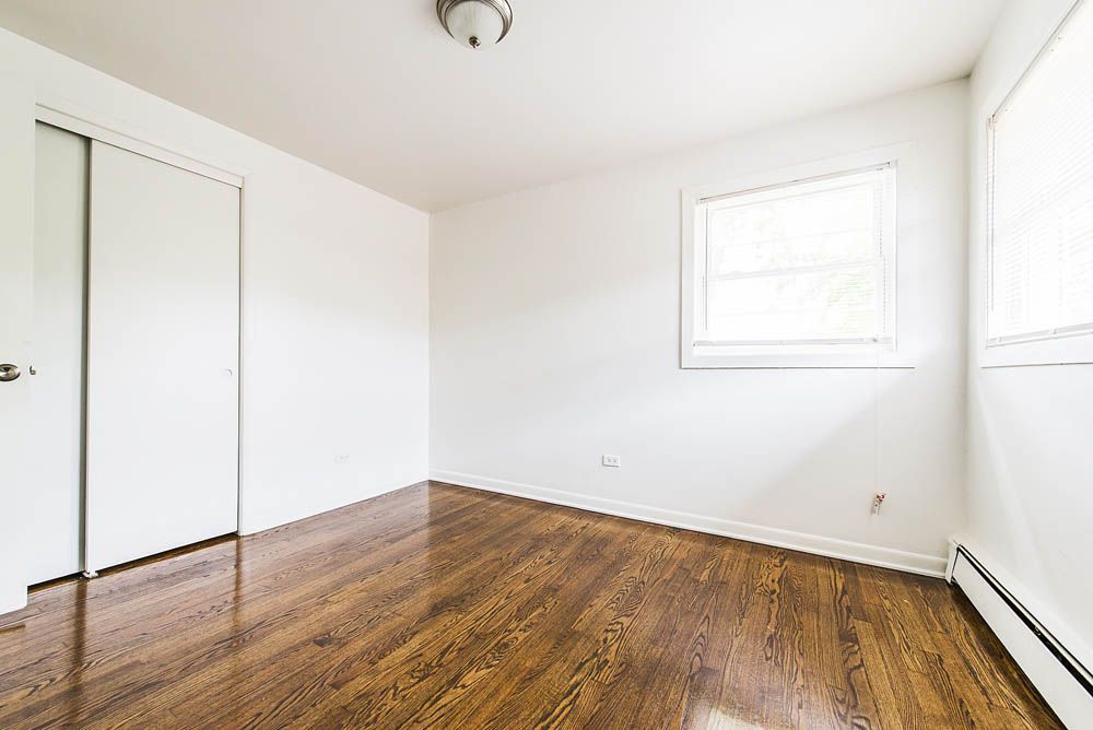 Empty bedroom with hardwood floors, white walls, and a window.