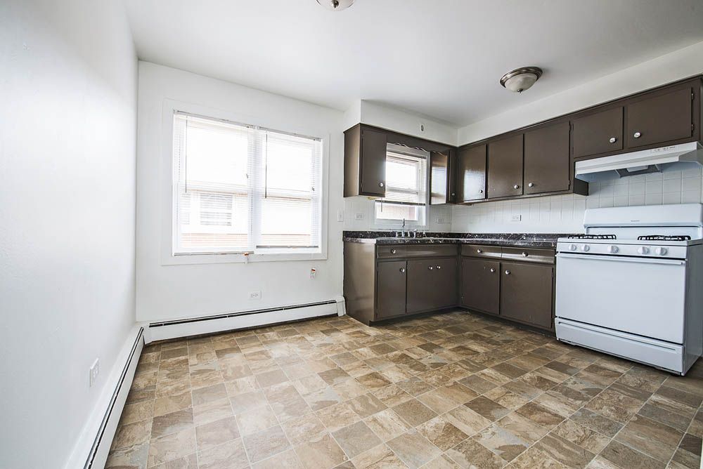 Empty kitchen with brown cabinets, white appliances, and beige patterned floor.