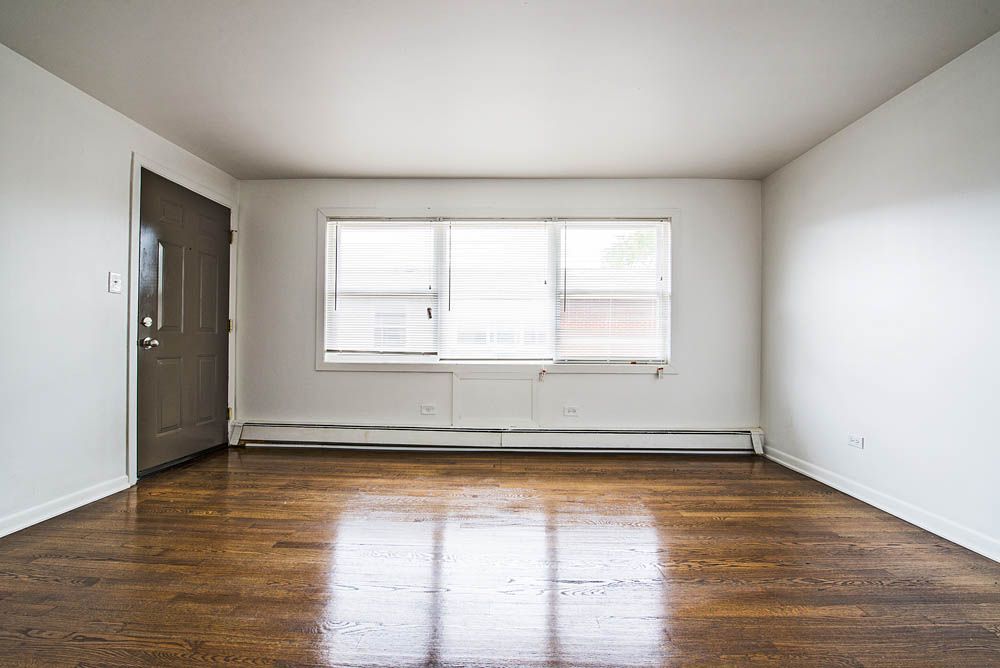 Empty room with hardwood floors, a door, and a window with blinds.