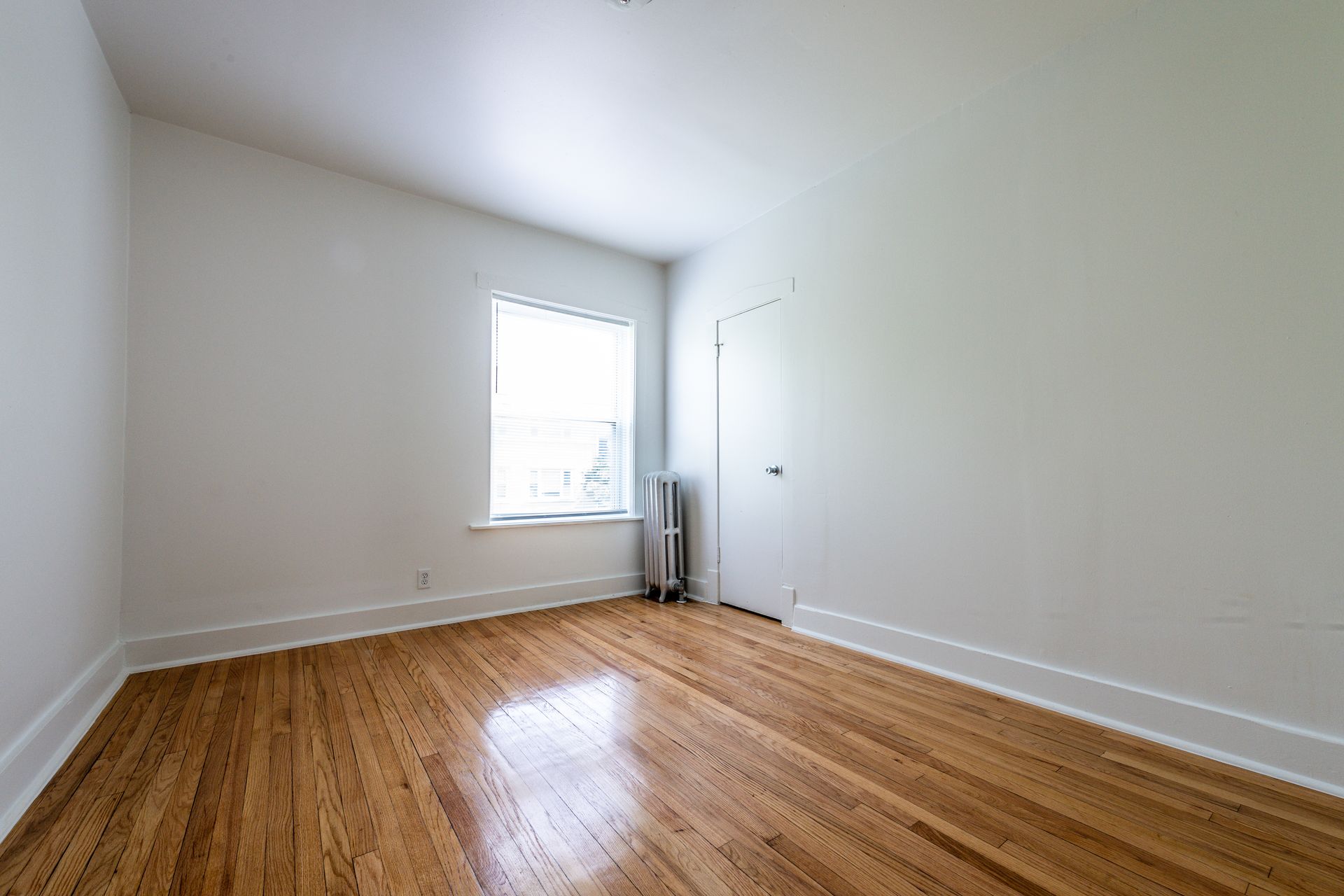 Empty room with hardwood floors, a window, and white walls.
