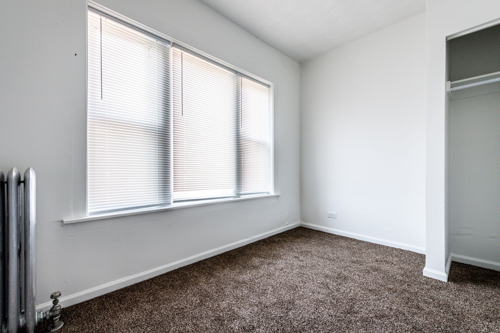 Empty bedroom with closed blinds, brown carpet, and a closet.