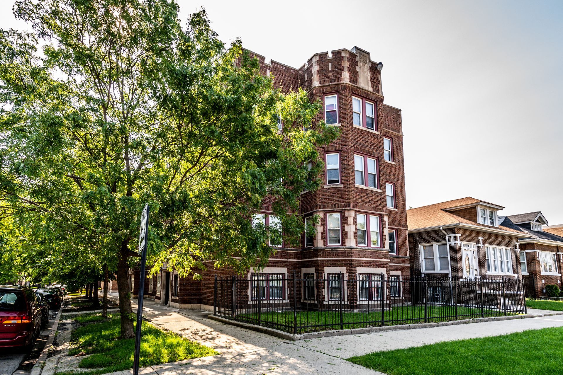 Brick apartment building on a corner lot, with a tree in front and a sunny sky.