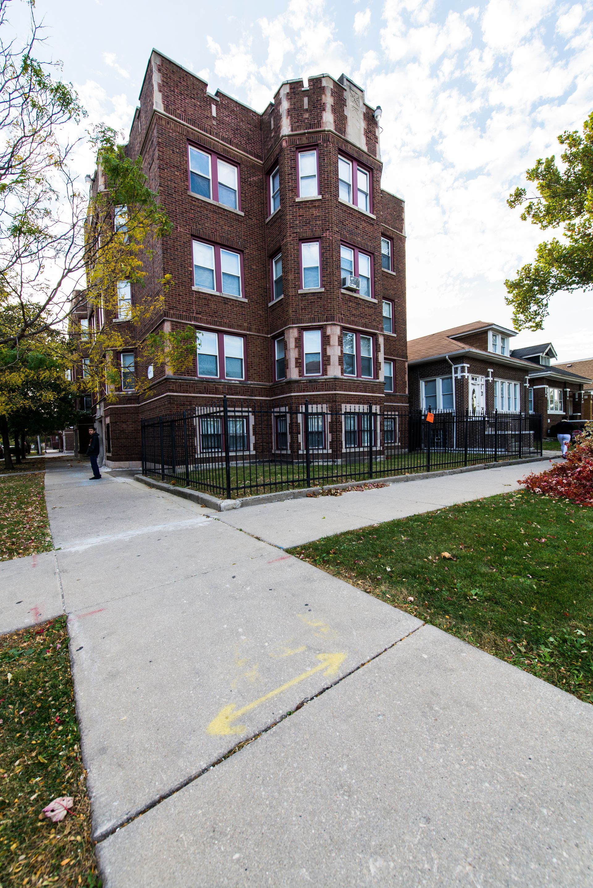 A tall brick apartment building with a turret, on a sidewalk with a yellow arrow.