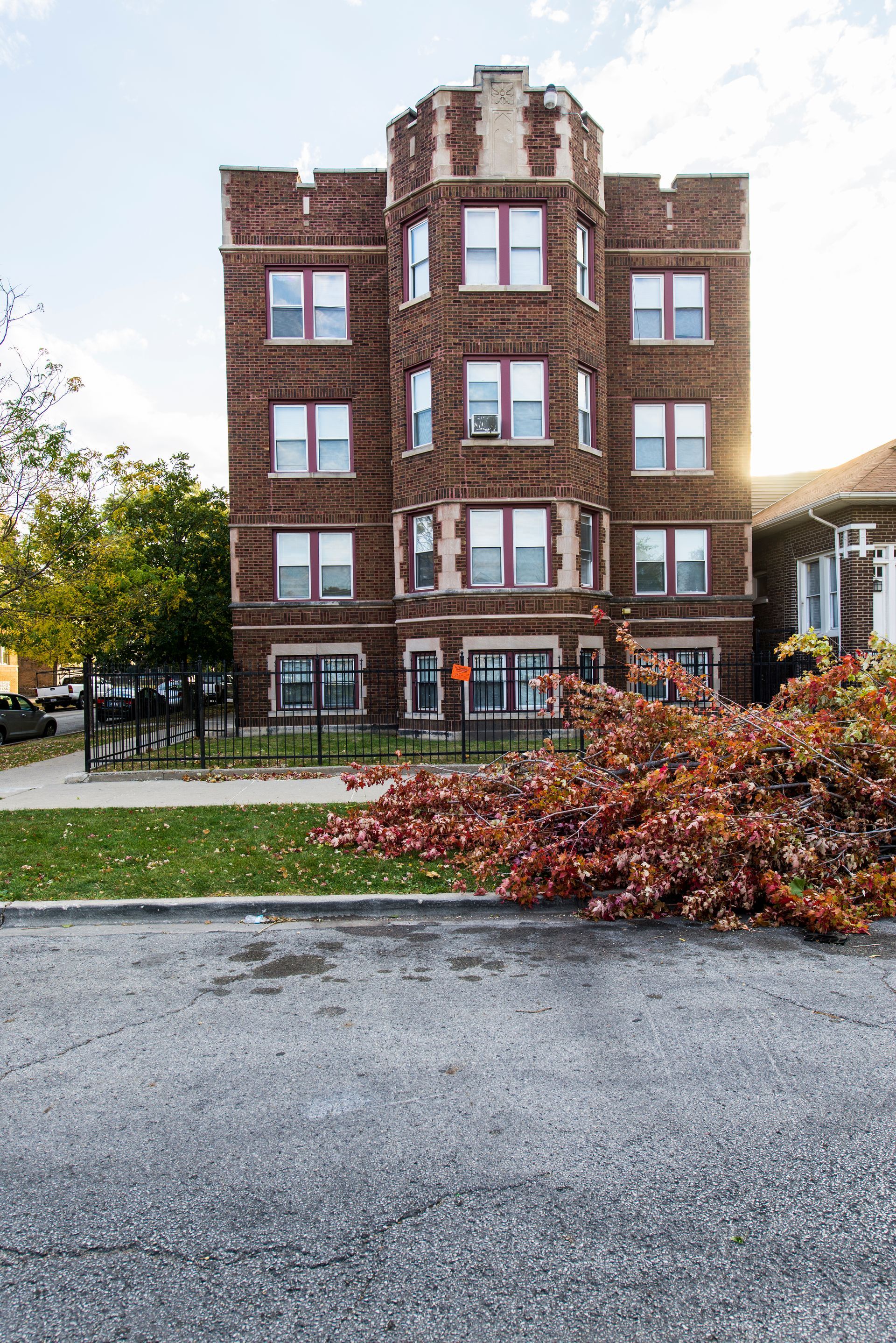 Brick apartment building with turret and red-trimmed windows; autumn foliage in foreground; bright sun.