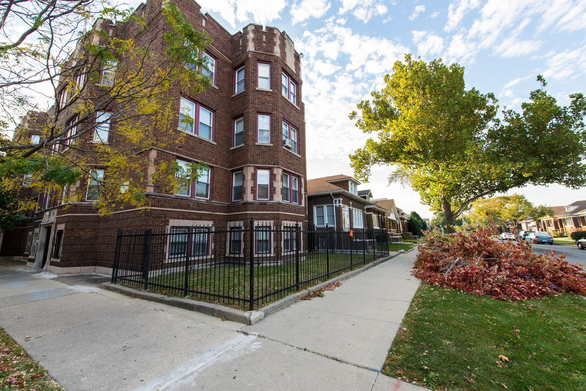 Brick apartment building with a wrought iron fence and sidewalk on a sunny day.