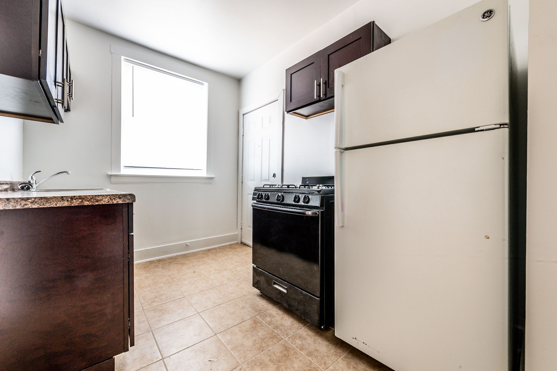 Kitchen with dark brown cabinets, a white refrigerator, a black stove, and a window.